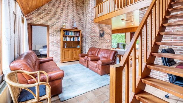 A spacious living area with a brick wall, wooden staircase, leather sofas, and a bookshelf. - Villa in St-idesbald Near Sea Beach (Koksijde)