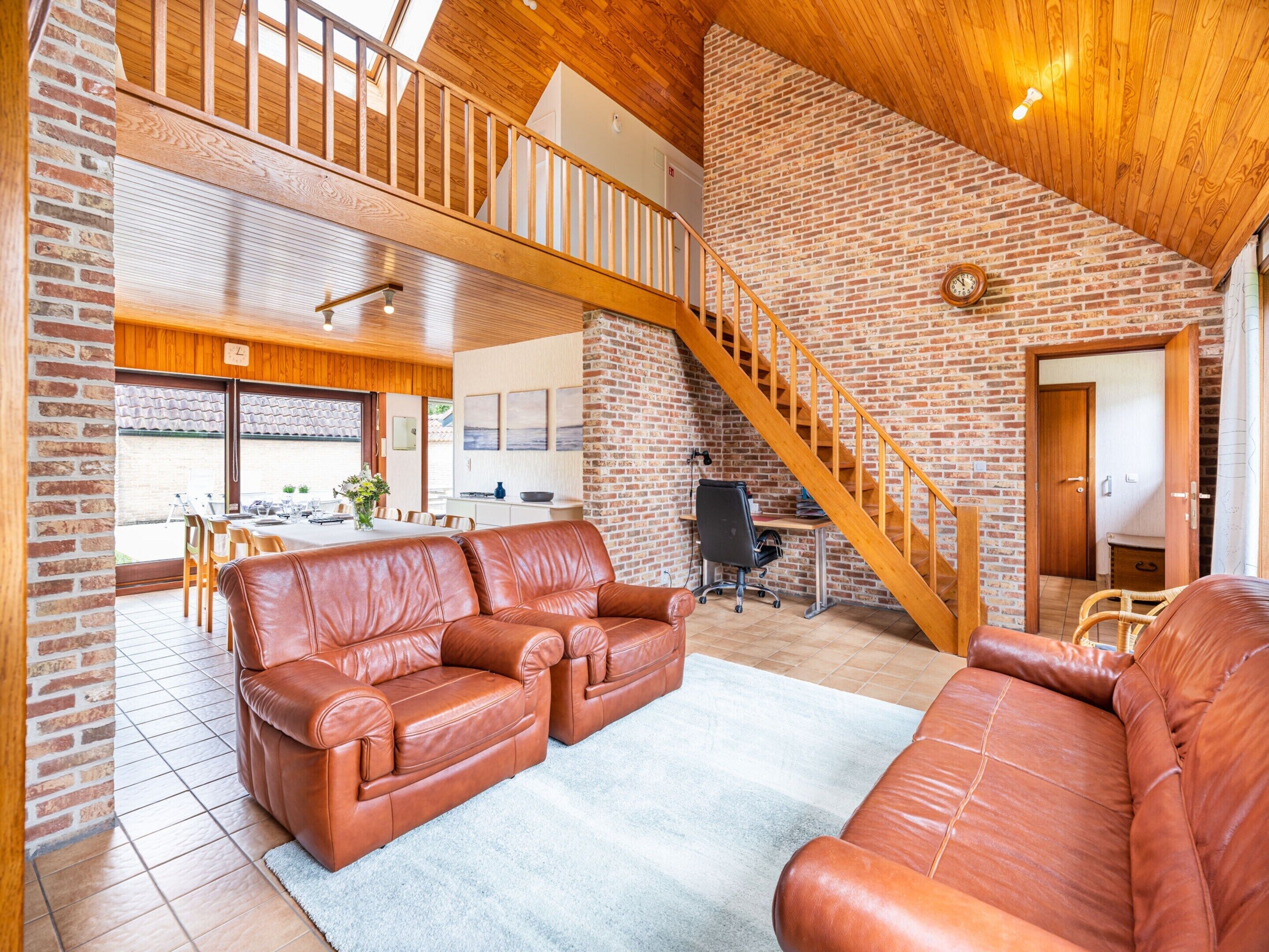 Un loft spazioso con soffitto alto, travi in legno a vista, una parete in mattoni e una scala.