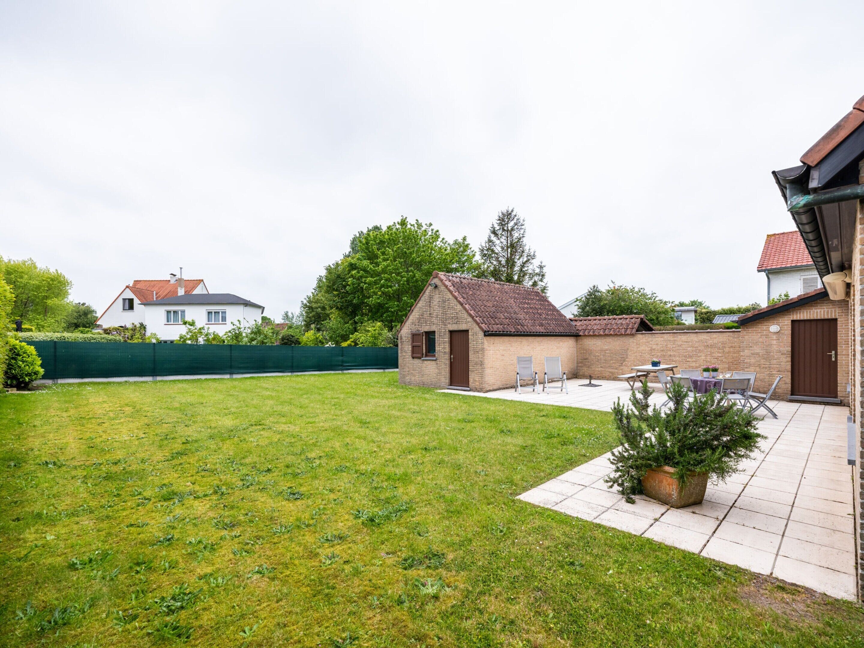 Ein Garten mit Terrasse, einem kleinen Backsteinhaus und einer Rasenfläche.