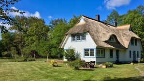 A traditional house with a thatched roof, surrounded by a well-maintained lawn and trees. - Holiday Apartment Dune Dream (Zingst)