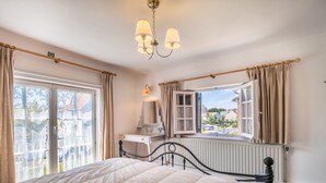 A bedroom with a bed, a dresser, a window with curtains, a radiator, and a chandelier. - Villa in Koksijde Near Zeedijk (Koksijde)