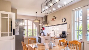 A kitchen with a wooden dining table set for tea, white cabinets, and a window with a view of greenery. - Villa in Koksijde Near Zeedijk (Koksijde)