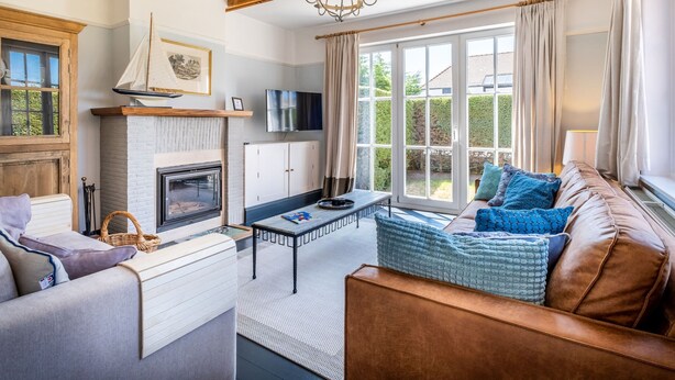A cozy living room with a fireplace, a television, and a comfortable seating area with cushions. - Villa in Koksijde Near Zeedijk (Koksijde)