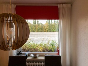 Ein Zimmer mit Blick auf ein Feld durch ein Fenster, inklusive Heizkörper und einem Tisch mit Stühlen.