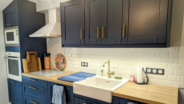 Een moderne keuken met donkerblauwe kastjes, een witte spoelbak en een ingebouwde oven.