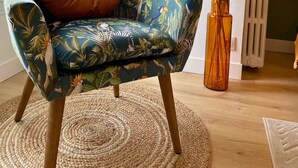 Een kamer met een fauteuil in tropisch thema, een geweven vloerkleed en een vaas met verenkrans.