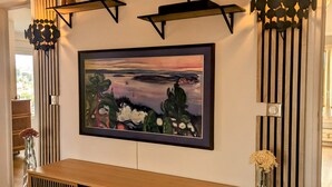 Een moderne woonkamer met een houten tv-meubel, een groot schilderij in lijst en decoratieve wandkunst.