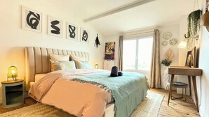 Een slaapkamer met een groot bed, een nachtkastje met een lamp, een hangplant en kunst aan de muur.