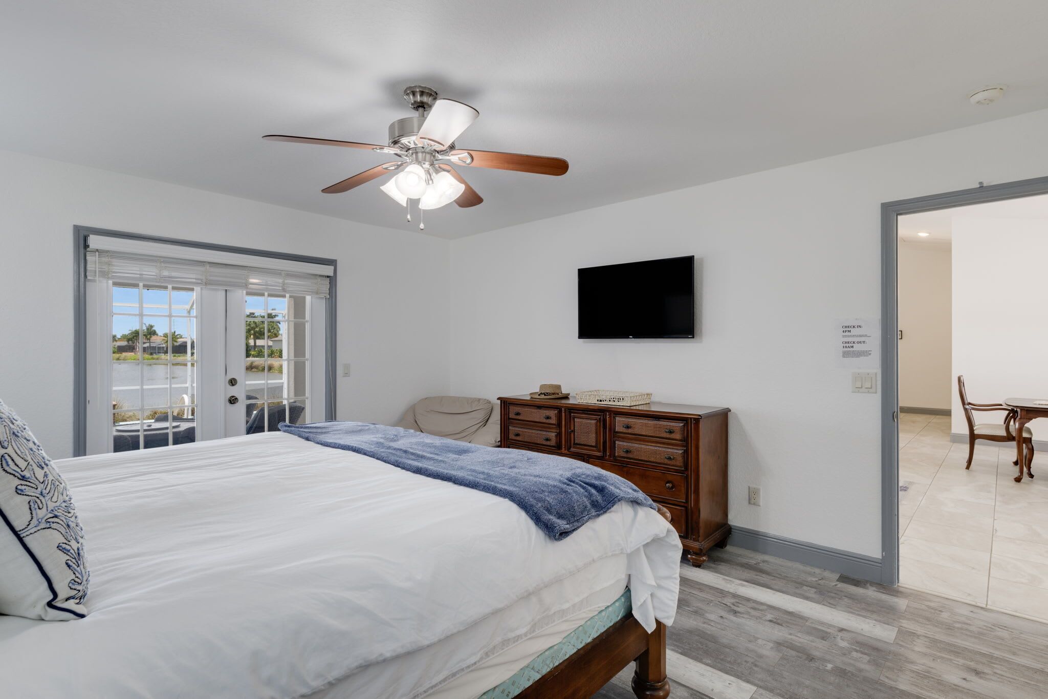 A bedroom with a bed, a ceiling fan, a TV, a dresser, and a sliding glass door leading to a balcony.