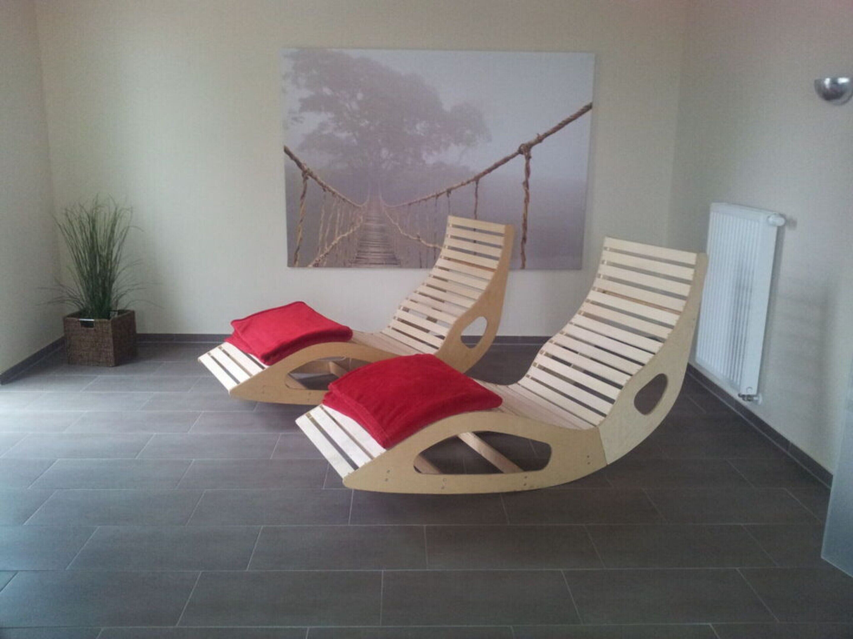 Zwei hölzerne Liegestühle mit roten Kissen, ein Blumentopf und eine Wandhängematte.