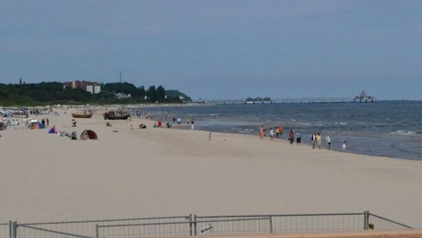 A beach with a metal railing, people, and a pier in the background. - Residence on Lake Balmer (Benz)