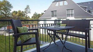 A balcony with wicker furniture and a table, overlooking a residential area with a house in the background. - Residence on Lake Balmer (Benz)