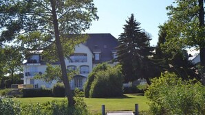 A pathway leading to a building with a white facade and multiple windows, surrounded by greenery and trees. - Residence on Lake Balmer (Benz)