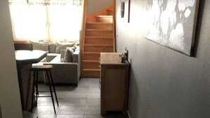 Um corredor estreito com chão de azulejos que leva a uma escadaria e a uma sala de estar com um sofá e uma pequena mesa.