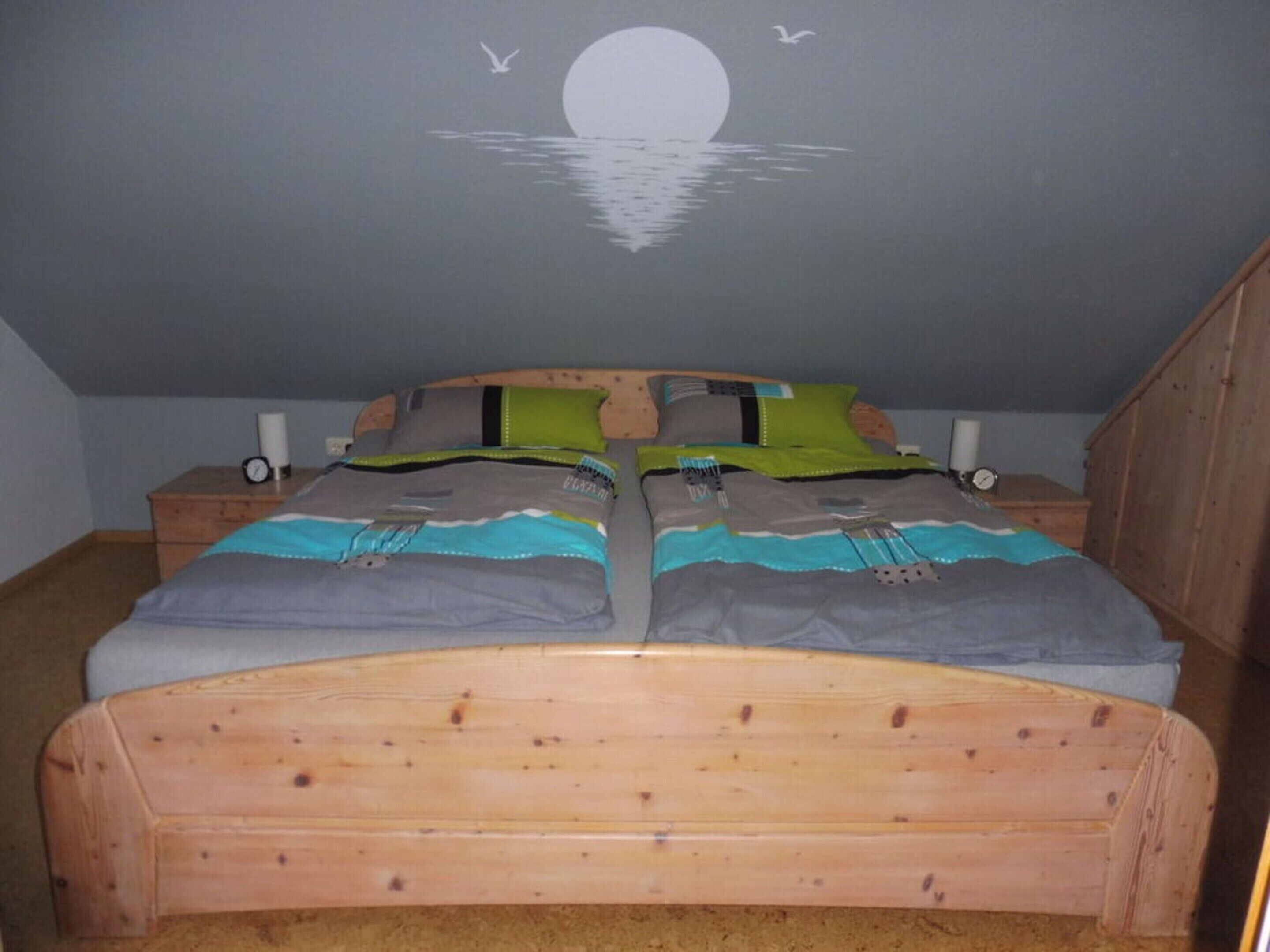 Un dormitorio con una cama de madera, dos mesitas de noche y un mural en la pared que muestra una luna sobre el agua.