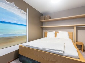 Une chambre à coucher avec un lit, une tête de lit en bois et une vue sur la plage, visible à travers une grande fenêtre.