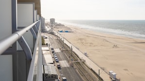 A beach view from a balcony with a road, beach, and buildings in the background. - Apartment on the 9th Floor With sea View (Middelkerke)