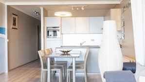 A modern kitchen with white cabinets, a built-in oven, and a dining area with a table and chairs. - Apartment on the 9th Floor With sea View (Middelkerke)
