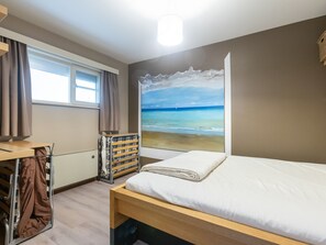 Un dormitorio con cama, ventana con cortinas, radiador y un mural de playa en la pared.