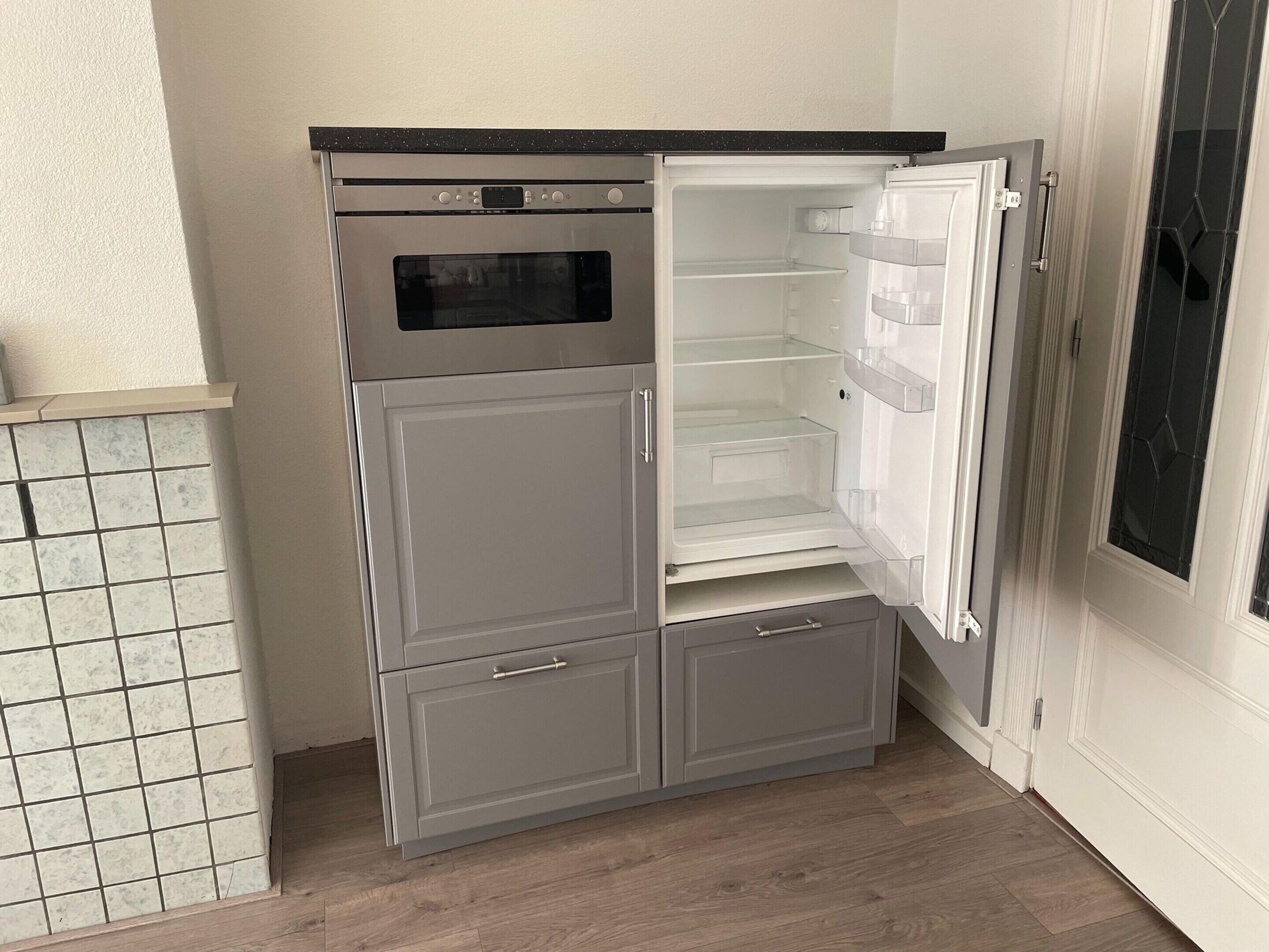 Une cuisine compacte dotée d’un four encastré et d’un réfrigérateur avec compartiment congélateur.