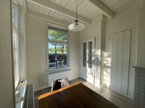 Una habitación con una mesa de comedor de madera, un radiador, una ventana con vistas a follaje y una puerta con un panel de vidrio.