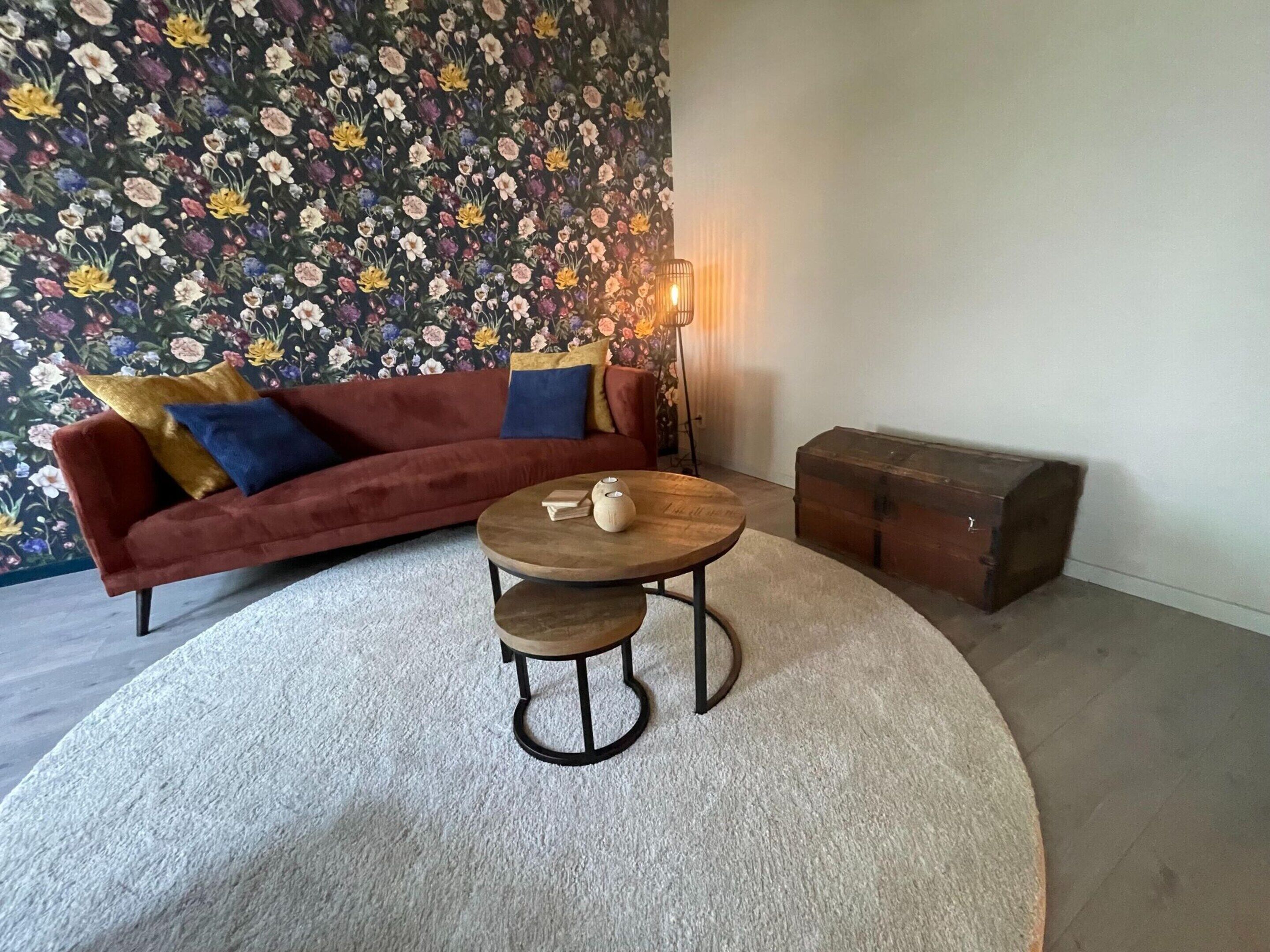 Una sala de estar con un sofá rojo, una mesa de centro redonda, un papel tapiz floral y una lámpara de pie.