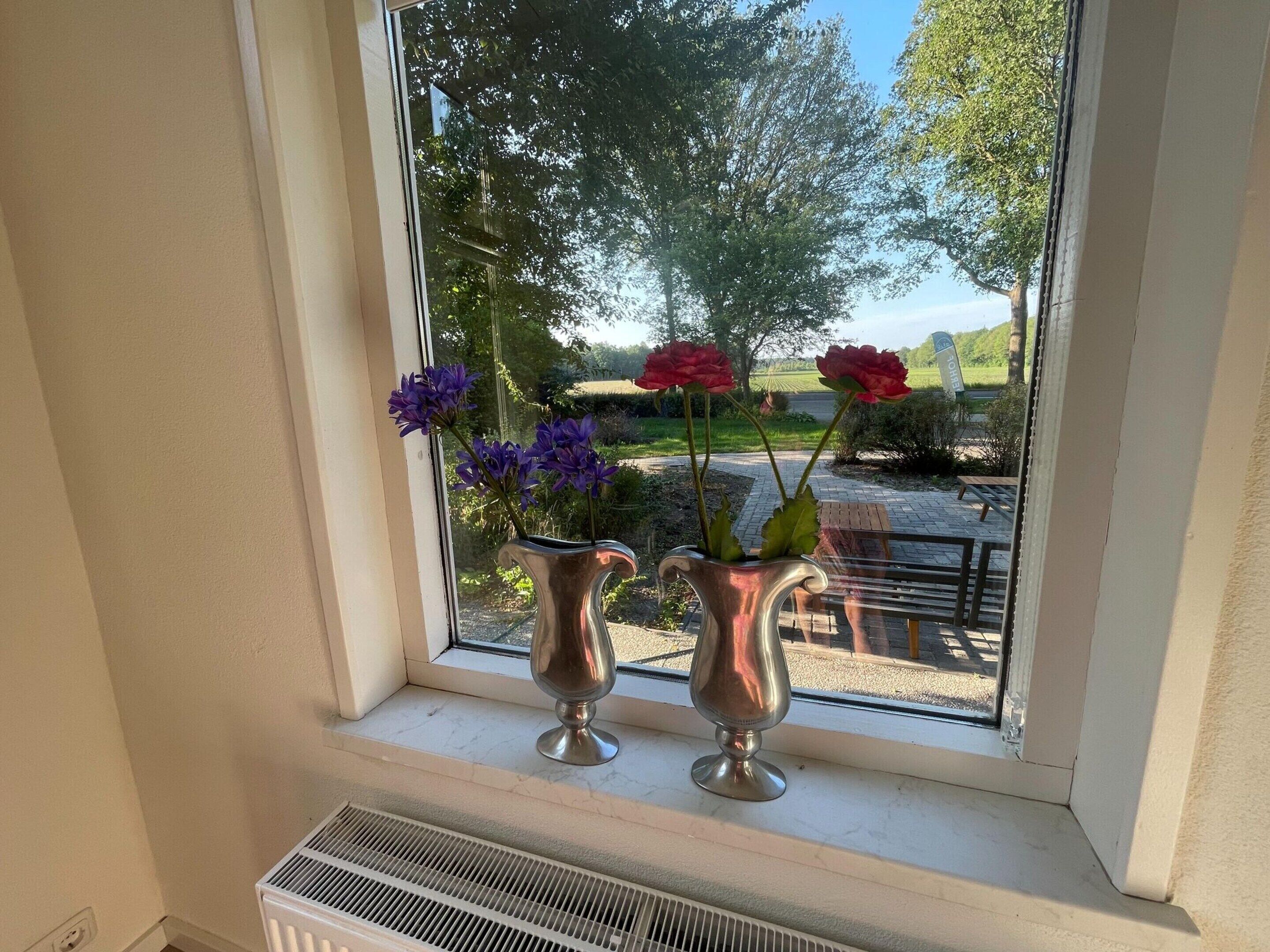 Two metallic vases with flowers on a windowsill.