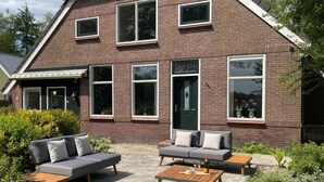 A two-story brick house with a patio area featuring a sofa set and a wooden table.