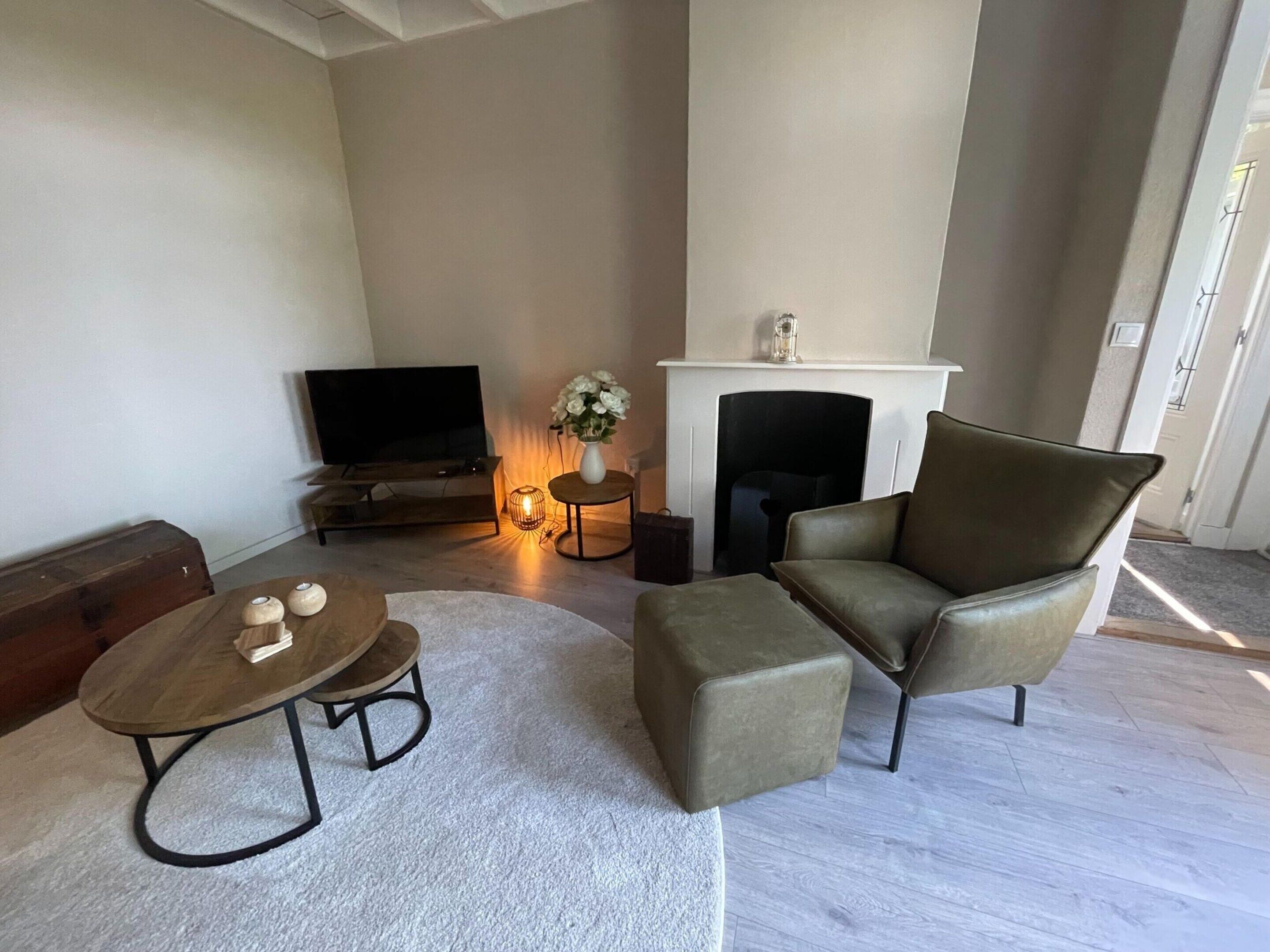 A modern living room with a flat-screen TV, a fireplace, a sofa, a coffee table, and a side table with a vase of flowers.