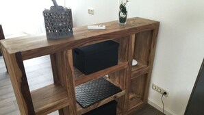 A wooden TV stand with shelves and storage compartments, a remote control, and a decorative vase. - Holiday Apartment Wurzburg (Würzburg)