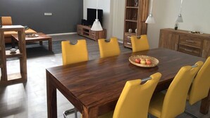 A dining area with a wooden table and yellow chairs, a television, and a bookshelf. - Holiday Apartment Wurzburg (Würzburg)