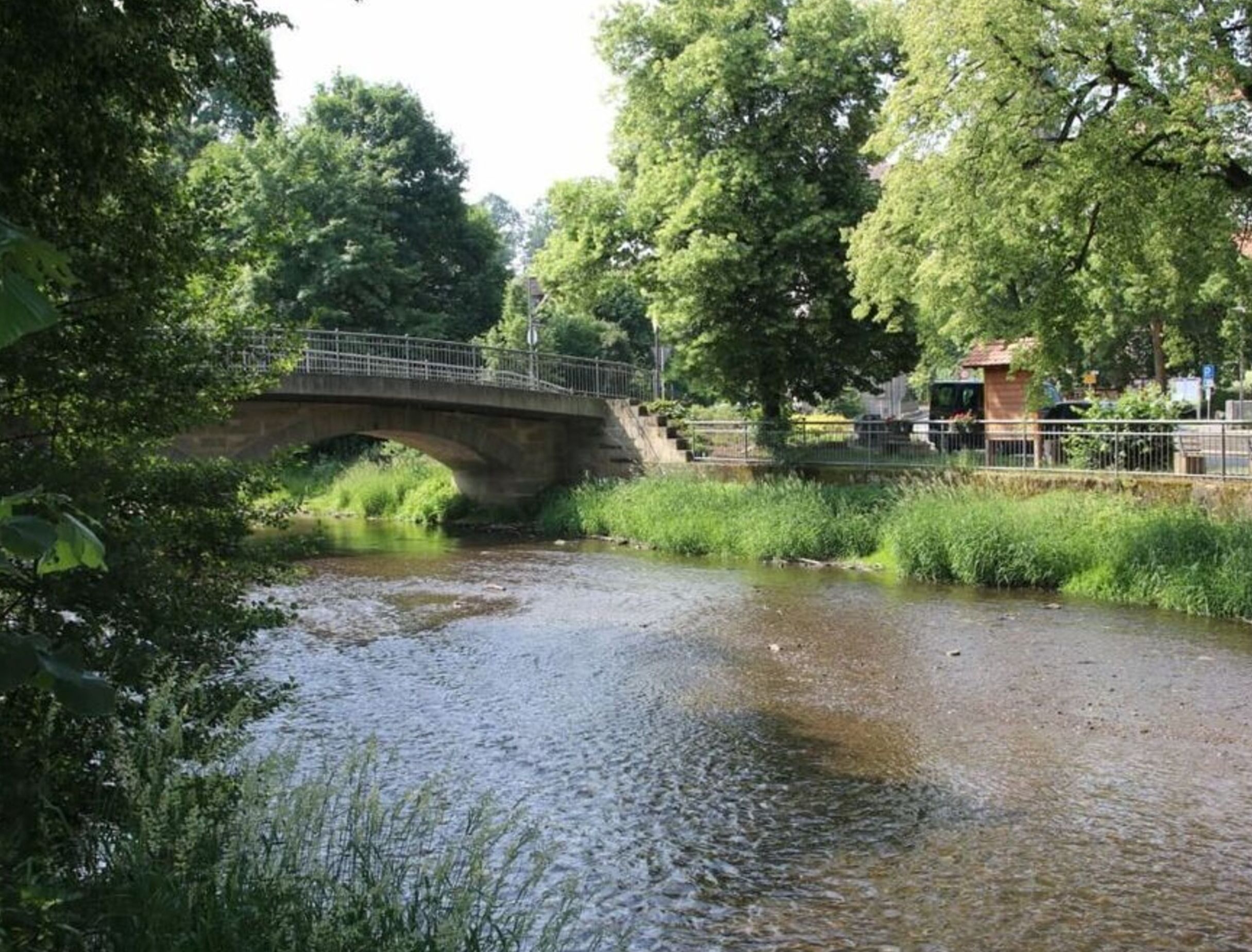 A stone bridge over a calm river with lush greenery on both sides.