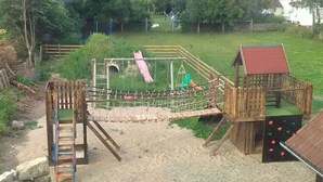 A playground with a rope bridge, a slide, and a small wooden structure with a red roof. - Nice Apartment in Himmelkron (Himmelkron)