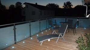 A wooden deck with a glass balustrade, outdoor seating, and string lights. - Nice Apartment in Himmelkron (Himmelkron)