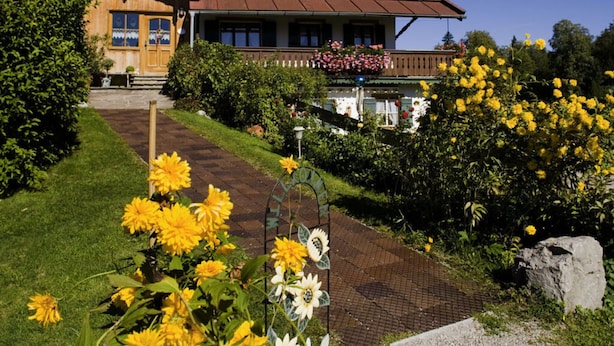 A traditional house with a tiled roof, a front porch, and a garden with yellow flowers. - Holiday Apartment Waxenstein (Lenggries)