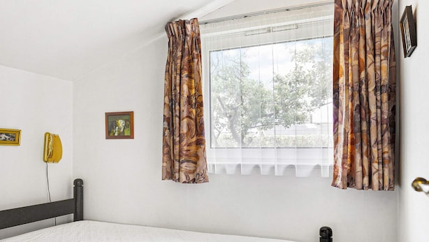A bedroom with a bed, a window with curtains, a wall-mounted telephone, and a picture frame. - 5 Person Holiday Home in Saeby (Sæby)