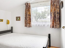Un dormitorio con cama, una ventana con cortinas, un teléfono montado en la pared y un marco de cuadros.