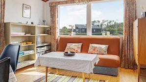 A cozy living room with a sofa, a table, a bookshelf, and a large window with a view of the outside. - 5 Person Holiday Home in Saeby (Sæby)