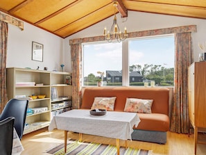 A cozy living room with a sofa, a table, a bookshelf, and a large window with a view of the outside. - 5 Person Holiday Home in Saeby (Sæby)