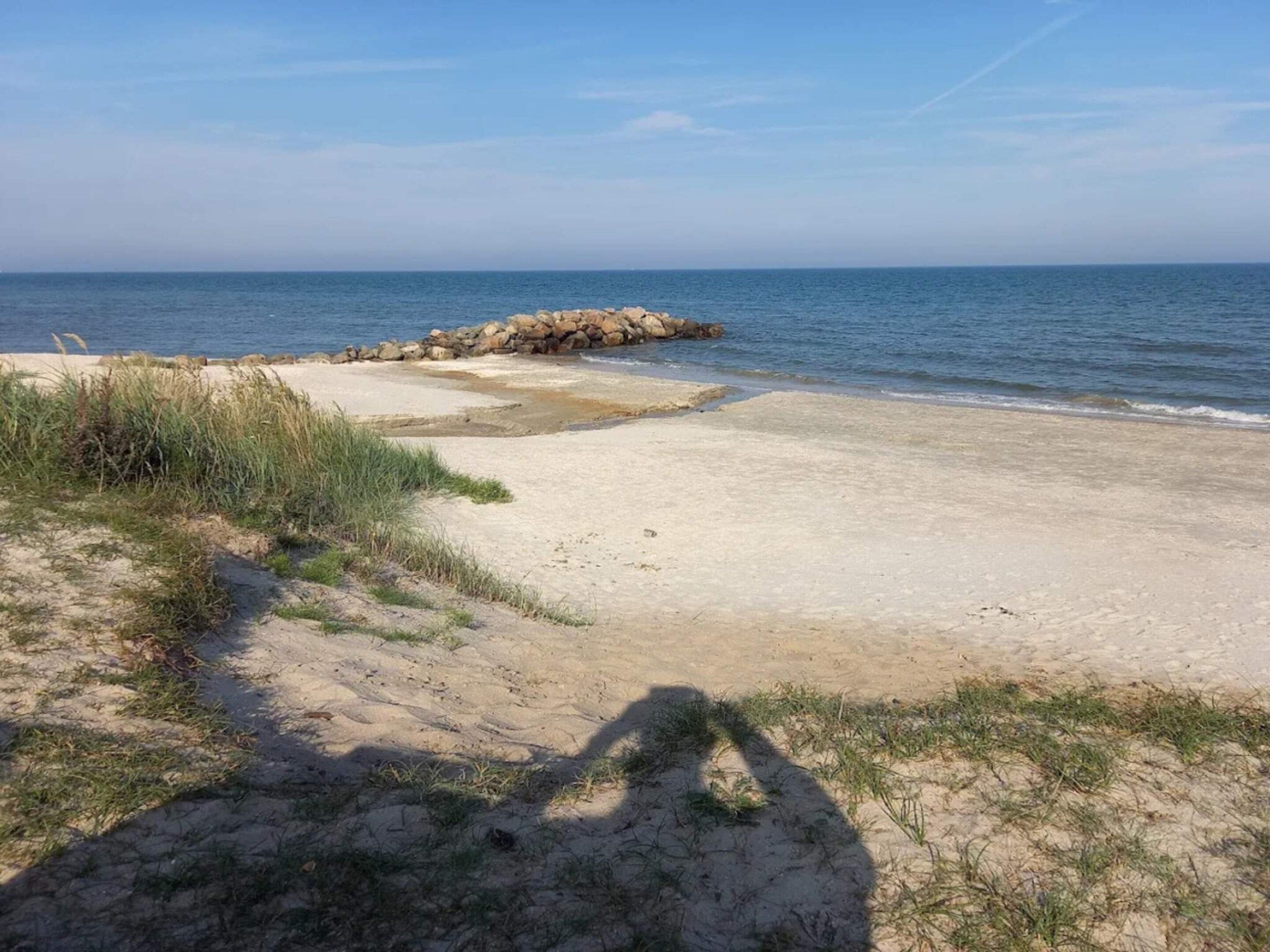 A beach with a rocky outcrop, sandy shore, and sparse grass.