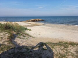 Una playa con un promontorio rocoso, orilla arenosa y poca hierba.