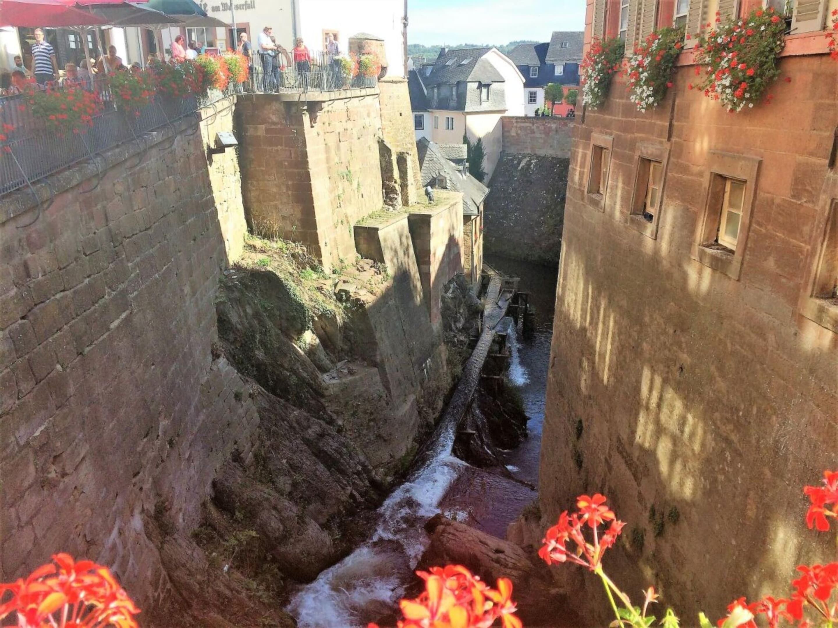 Eine schmale Steinbrücke über einen Wasserkanal, gesäumt von Gebäuden mit Blumenkästen.