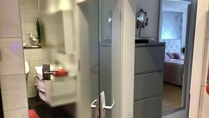 A modern bathroom with a glass partition, a toilet, a sink, and a mirror. - Holiday Apartment Gertie (Saarburg)