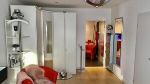 A modern hotel room with a bed, a red armchair, a small table with a candle, and a white wardrobe. - Holiday Apartment Gertie (Saarburg)