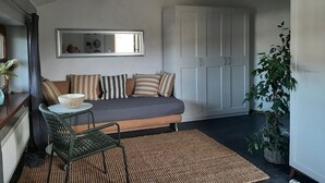 A cozy living room with a sofa, a small table, a chair, a ceiling fan, and a large mirror.