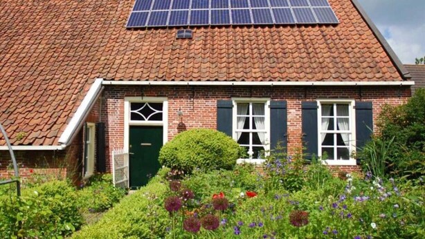 A traditional brick house with a tiled roof, a green door, and a garden with various plants and flowers. - Swanenhuus Modern Retreat (Krummhoern)