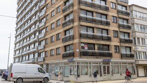 Ein mehrgeschossiges Gebäude mit Balkonen, einem Ladenbereich im Erdgeschoss und einem geparkten Lieferwagen.