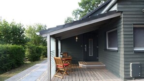 A covered outdoor deck with a table and chairs, a door, and a window. - Holiday Home Naturally Good (Voehl)