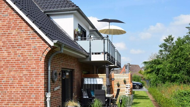 A brick building with a balcony, outdoor seating, and potted plants. - Beach Apartment in Schleswig-holstein (Westerdeichstrich)