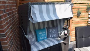 A patio seating area with a striped cushion, a pillow with a quote, and a bottle of wine on a small table. - Beach Apartment in Schleswig-holstein (Westerdeichstrich)